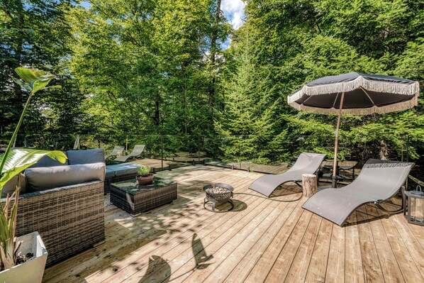 A wooden deck with outdoor furniture, including a sofa, lounge chairs, and a fire pit. - Chalet La Trepa | Ski, Spa, Sun Deck, Fire pit (Chertsey)