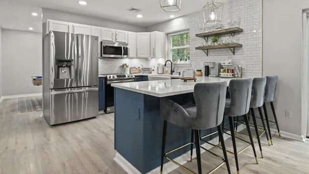 A modern kitchen with stainless steel appliances, a central island with bar stools, and a brick accent wall.