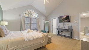 A bedroom with a large bed, a TV, a console table, and a window with curtains.