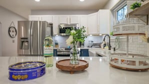 A modern kitchen with white cabinets, a stainless steel refrigerator, a vase with flowers, a bottle of olive oil, and a can of cookies.