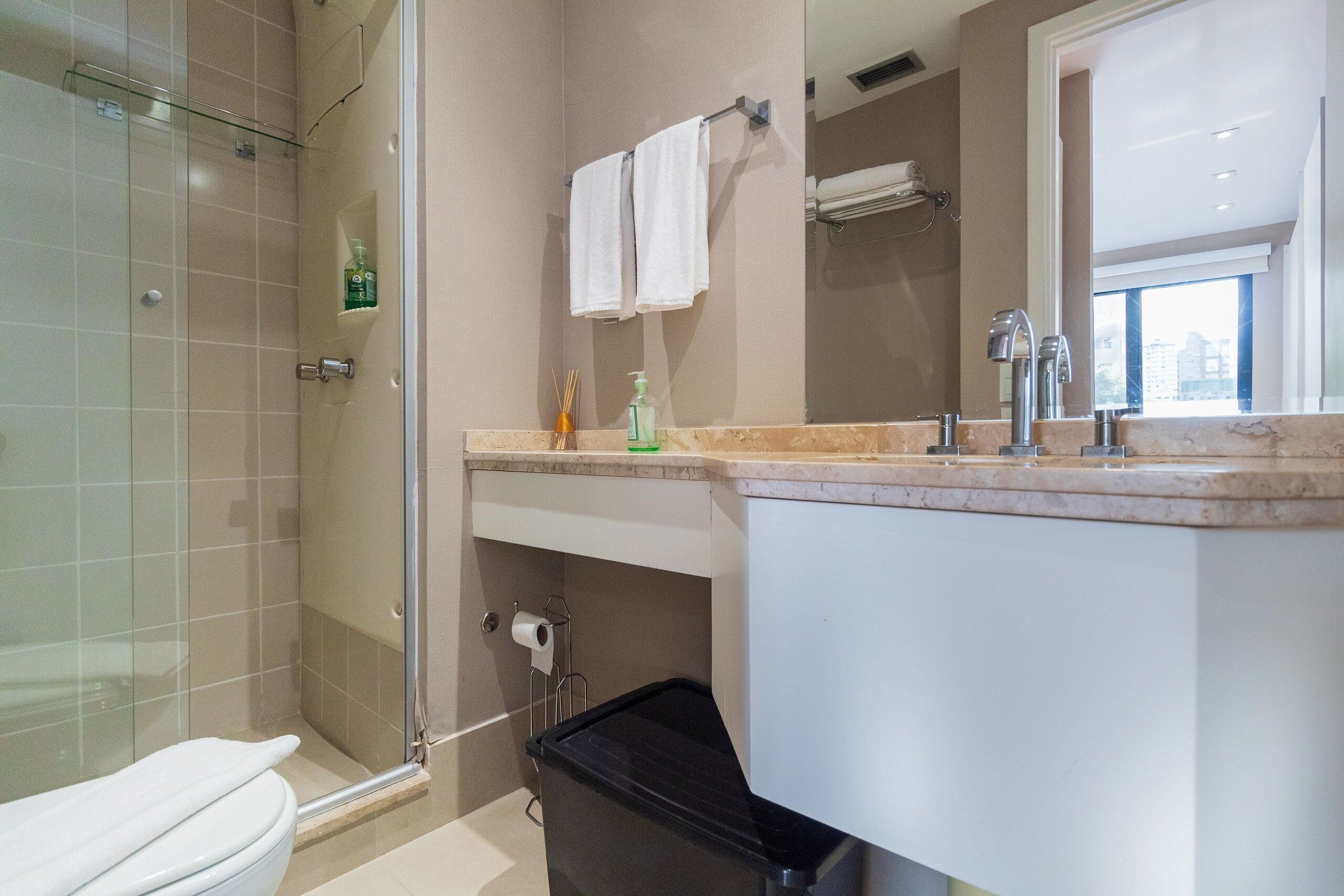 Une salle de bain moderne avec une douche à parois de verre, des toilettes, un lavabo avec un miroir et une poubelle.