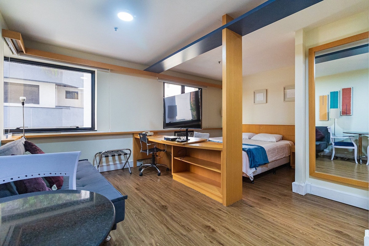 Una habitación de hotel pequeña con una cama, un escritorio con ordenador, una silla y una mesita.