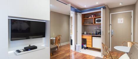 A compact living space with a flat-screen TV, a kitchenette, a dining area, and a sofa.