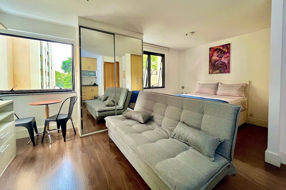 Un espacio habitable compacto con un sofá, una mesita y una silla. Cuenta con una pequeña cocina americana y una ventana.