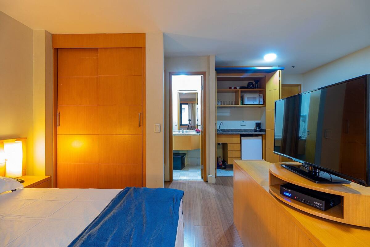 Una habitación de hotel con cama, televisión, escritorio y kitchenette.