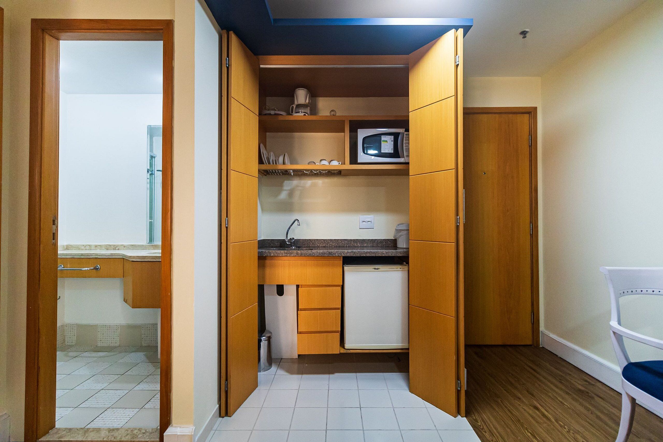 A compact kitchen with wooden cabinets, a microwave, and a small refrigerator.