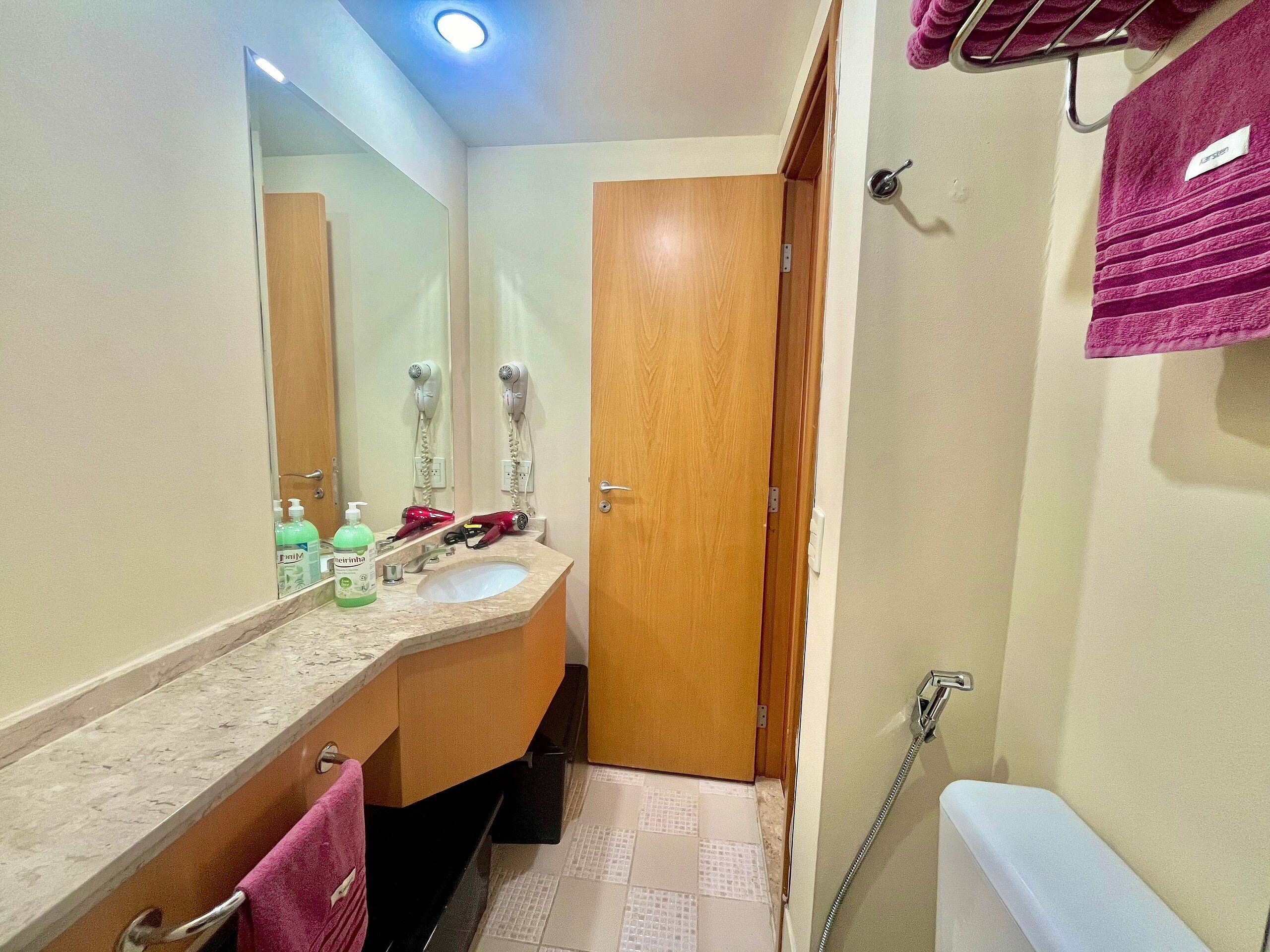 A bathroom with a sink, mirror, hairdryer, and towel rack.