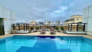 Une piscine sur le toit, agrémentée de deux chaises longues et de plantes en pot, le tout entouré d’immeubles.