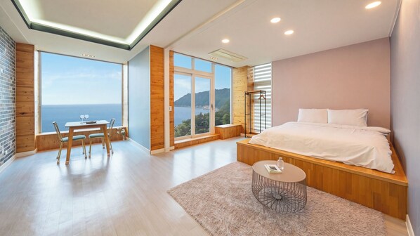 A bedroom with a large bed, a bedside table, and a view of the sea.