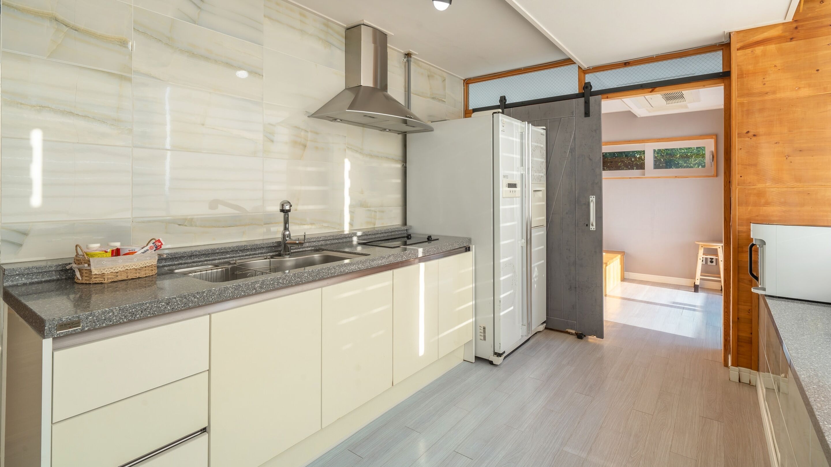 A modern kitchen with a marble backsplash, stainless steel appliances, and a sliding wooden door leading to another room.