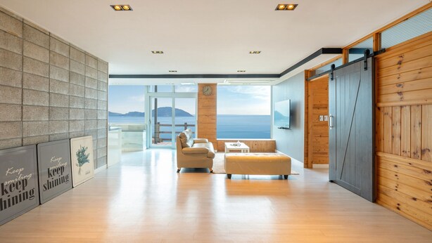 Un salon moderne doté d’une grande fenêtre donnant sur la mer, d’un canapé, d’une table basse et de murs en bois.