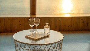 A round table with a book and two glasses, a bottle, and a wooden wall in the background. - Geoje Inbito Pension (Geoje)