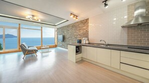 A modern kitchen with a large window overlooking the sea, a built-in oven, and a dining area with a view. - Geoje Inbito Pension (Geoje)