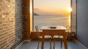 Un coin repas avec une table et des chaises, donnant sur une grande fenêtre qui offre une vue sur la mer au coucher du soleil.