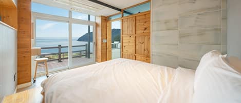Une chambre avec un grand lit, des boiseries, une vue sur la mer et un balcon.