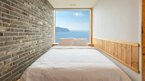 A bedroom with a brick wall, wooden headboard, and a large window overlooking the sea. - Geoje Inbito Pension (Geoje)
