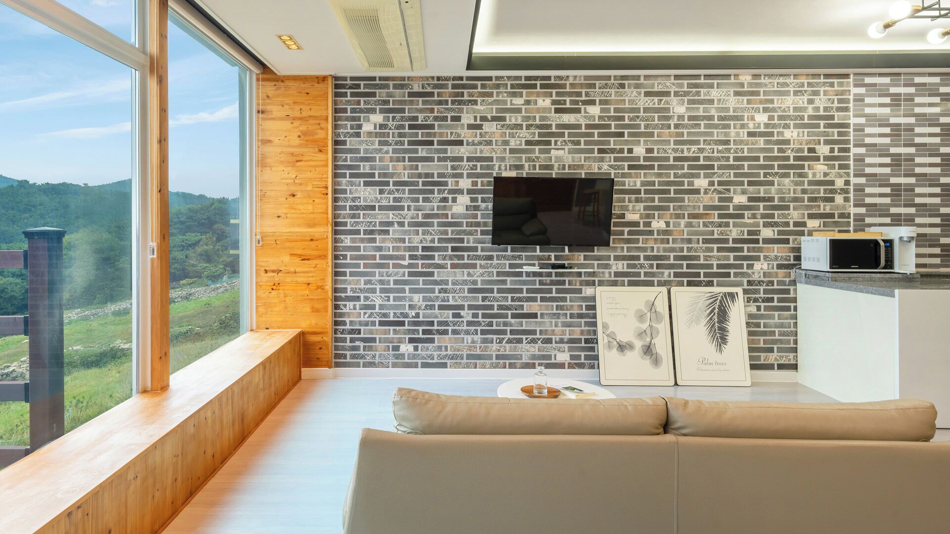 Ein modernes Wohnzimmer mit großem Fenster, Ziegelwand, Flachbildfernseher, Mikrowelle und einer Couch.