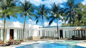A resort pool area with palm trees, a white building, and a clear blue sky. - Casa Marta Hotel (Iloilo)