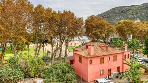 A pink building with a tiled roof, surrounded by trees and a beach in the background. - Ribas Machico, a Home in Madeira (Machico)