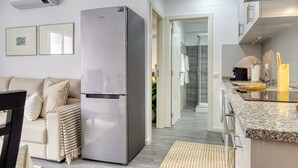 A modern kitchen with a built-in refrigerator, a dining area with a sofa and chairs, and a visible bathroom with a shower. - Ribas Machico, a Home in Madeira (Machico)