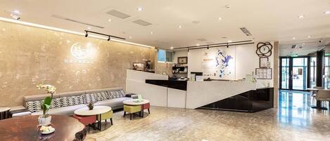 A modern hotel lobby with a reception desk, seating area, and a map on the wall.