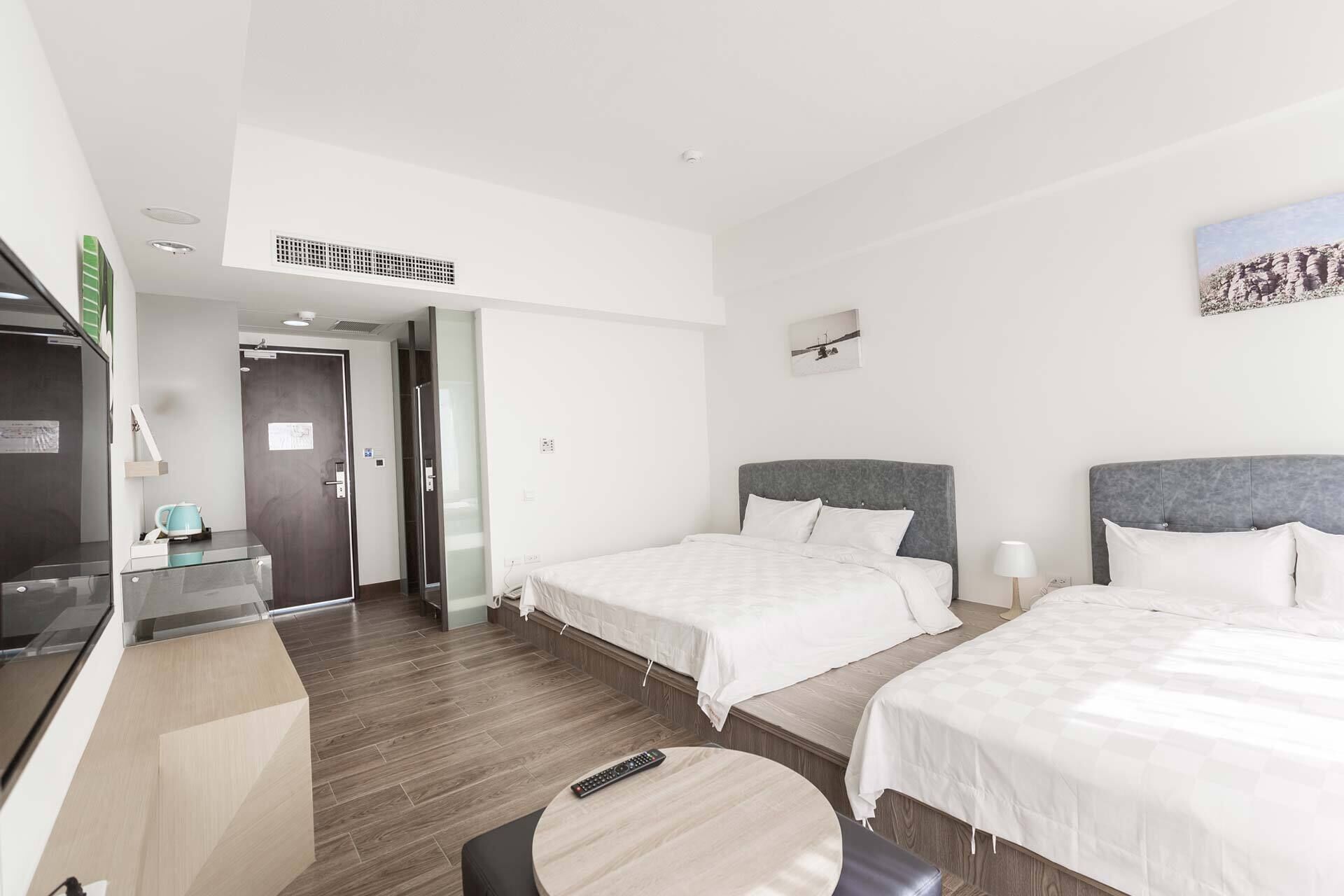 A hotel room with two beds, a desk, a chair, and a small table.