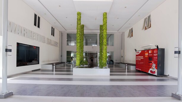 Eine moderne Lobby mit einem großen digitalen Bildschirm, einem Empfangsbereich und einer Treppe zu den oberen Etagen.
