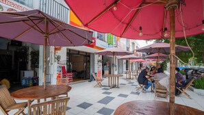 Ein Straßencafé mit Holztischen und -stühlen, überdacht mit roten Sonnenschirmen und einem Schachbrettmuster-Boden.