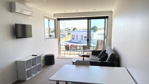 Ein modernes Wohnzimmer mit einem weißen Tisch, schwarzen und weißen Stühlen, einem grauen Sofa und einem an der Wand befestigten Fernseher.