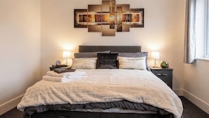 A hotel room with a large bed, two bedside tables with lamps, a wall art piece, and a window with curtains. - 2 Bed, Sleeps 4, Pet Friendly, Free Parking (Rotherham)