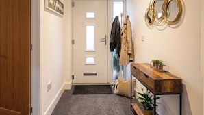 A hallway with a wooden door, a coat rack with jackets, a console table with plants, and a wall-mounted mirror. - 2 Bed, Sleeps 4, Pet Friendly, Free Parking (Rotherham)