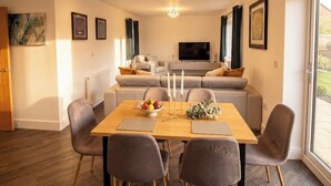 A modern living room with a dining table, grey sofas, a TV, and a large window. - 2 Bed, Sleeps 4, Pet Friendly, Free Parking (Rotherham)