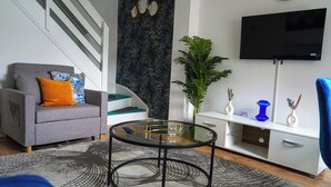 Een moderne woonkamer met een grijze bank, een glazen salontafel, een witte kast, een televisie en een trap.