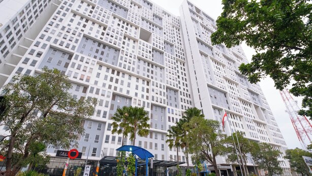 A modern high-rise building with a grid-like facade, a covered entrance area with palm trees, and a sign indicating a hotel. - Apartemen Patra Land Urbano By Abdihome (Bekasi)