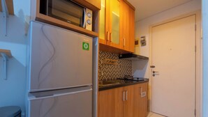 A compact kitchen with a refrigerator, microwave, and stove. There is a tiled backsplash and wooden cabinets. - Apartemen Patra Land Urbano By Abdihome (Bekasi)