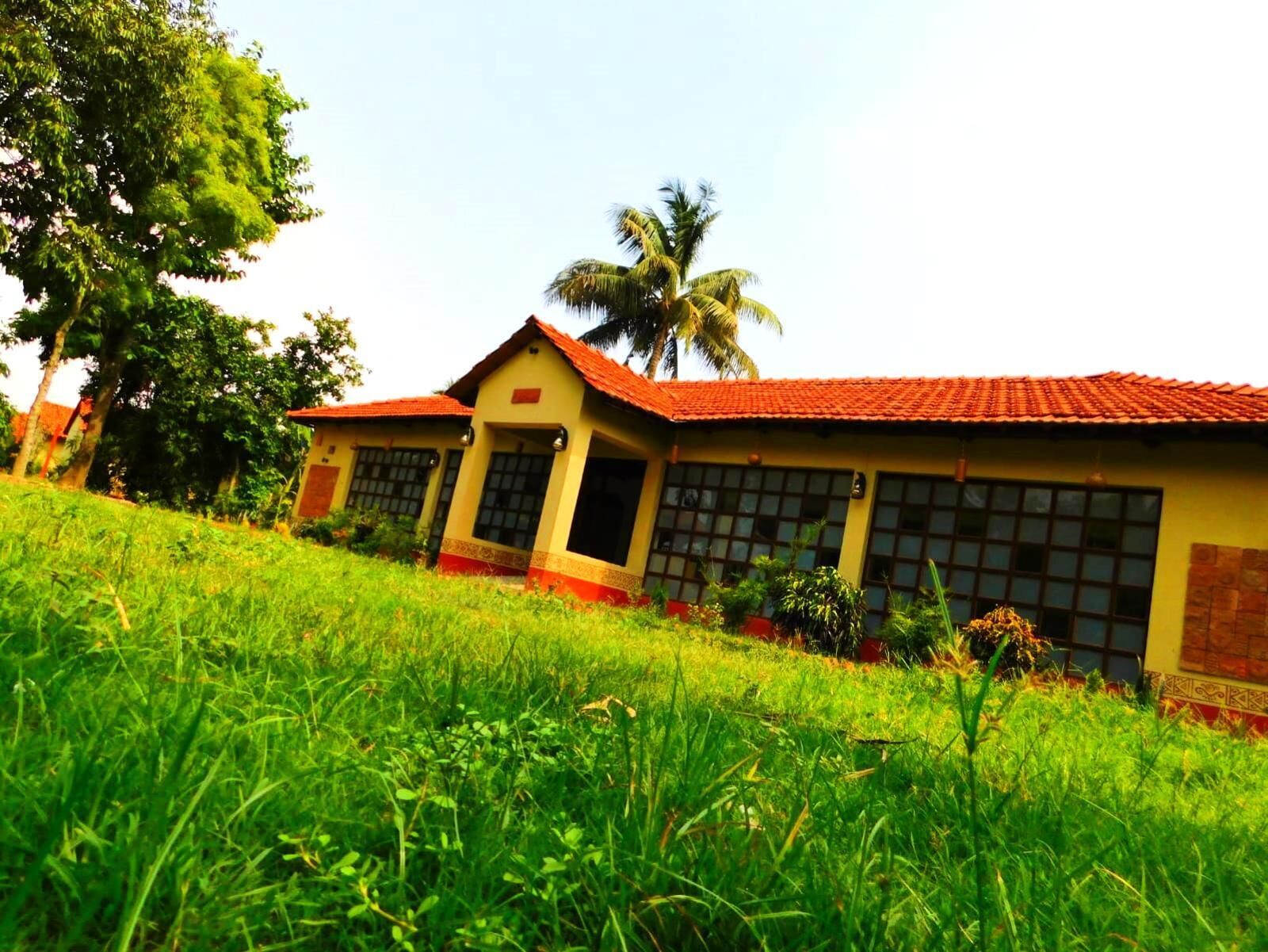 A two-story building with a red-tiled roof, surrounded by lush green grass and palm trees.