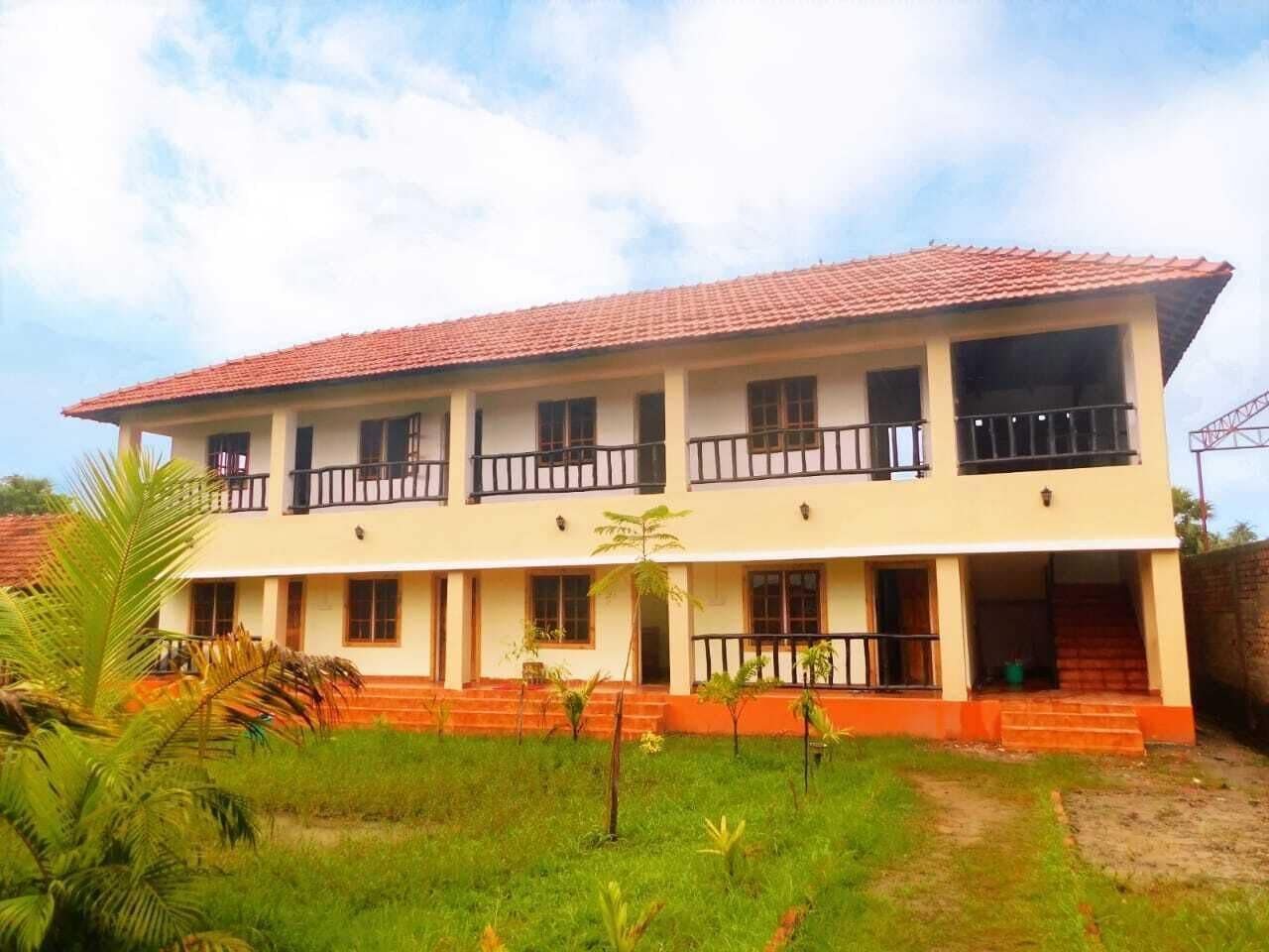 A two-story building with a red-tiled roof, multiple balconies, and a front entrance with steps.