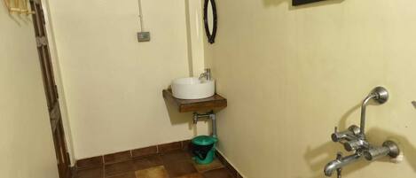 Un baño pequeño con un lavamanos blanco, un bote de basura verde, una ducha y un perchero para toallas.