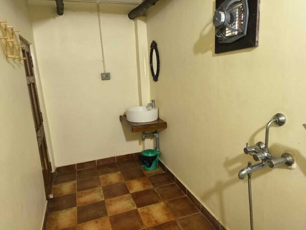 A small bathroom with a white sink, a green trash bin, a shower, and a towel rack. - Gram Bangla Retreat (Alipur)