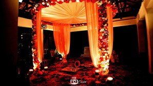 An ornate canopy with draped fabric and floral arrangements, a patterned carpet, and candles on the floor. - Gram Bangla Retreat (Alipur)