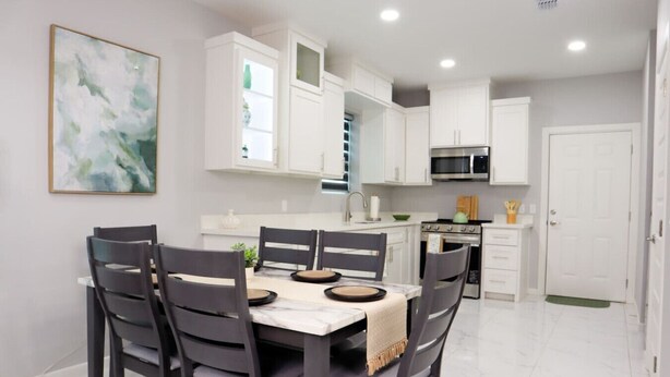 A modern kitchen with white cabinets, a stainless steel microwave, and a dining area with a marble table and dark chairs. - Vista Verde Suite In Alamo Tx (Alamo)