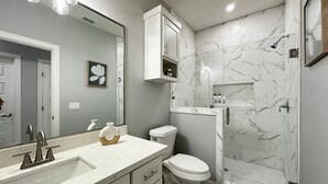 A modern bathroom with a white sink, vanity, and toilet. It features a large mirror, marble walls, and a shower area. - Vista Verde Suite In Alamo Tx (Alamo)