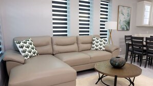 A beige sectional sofa with patterned pillows, a round coffee table with a vase, and a dining area with chairs and a table. - Vista Verde Suite In Alamo Tx (Alamo)