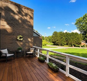 Eine Holzterrasse mit Gartenmöbeln, eine Backsteinmauer und Blick auf eine grüne Landschaft.