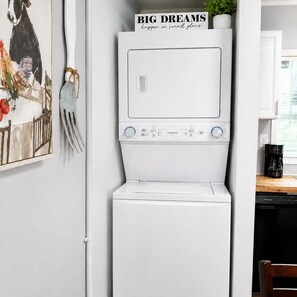 Eine kompakte Küche mit weißen Geräten, einer Kaffeemaschine und einem gerahmten Bild an der Wand.
