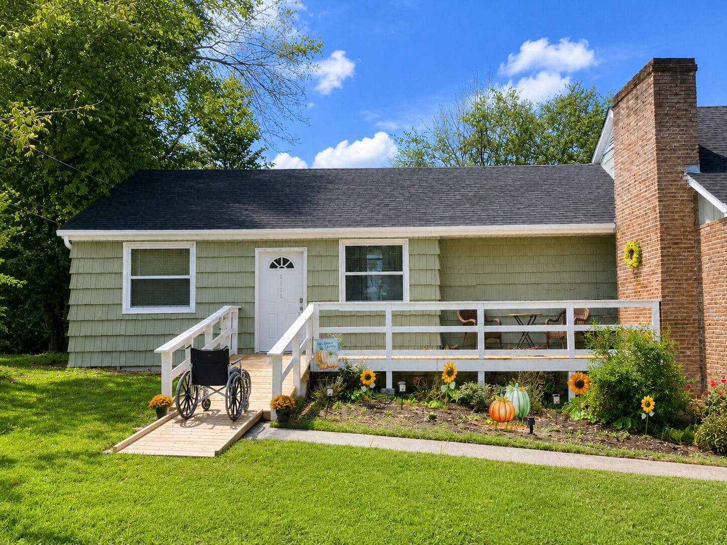 A single-story house with a front porch, a wheelchair ramp, and a garden with sunflowers and pumpkins.