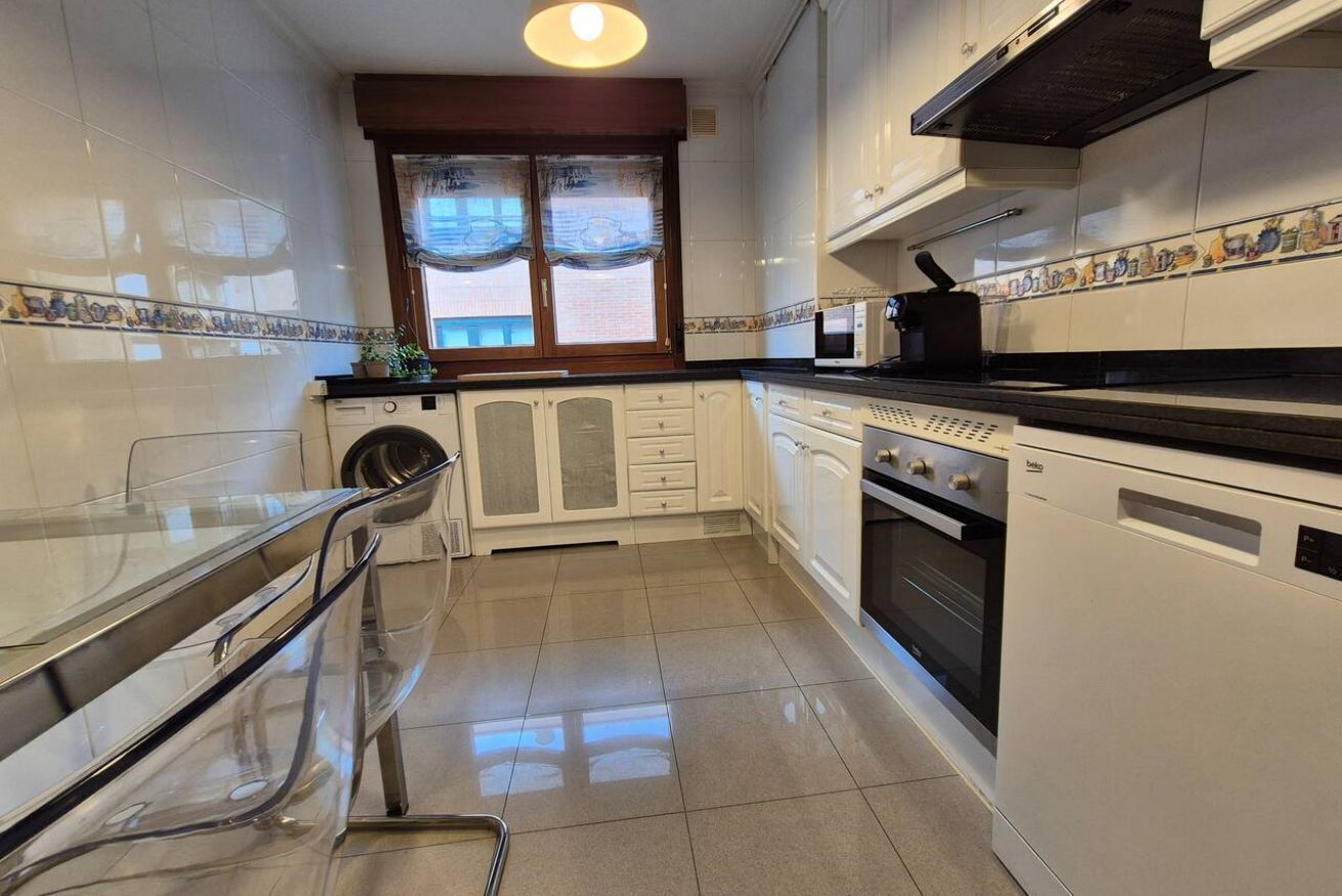 Een compacte keuken met een wasmachine, oven en een glazen eettafel.