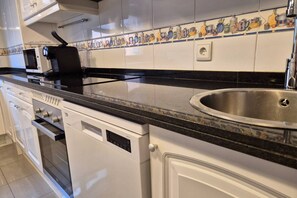 A kitchen with white cabinets, a black countertop, a stainless steel sink, and a microwave. - 1A137 Apartamento con encanto puerto deportivo (Gijón)