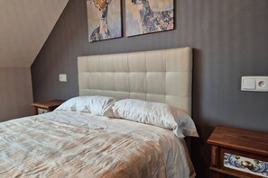A bedroom with a large bed, a headboard, two nightstands, and artwork on the wall.
