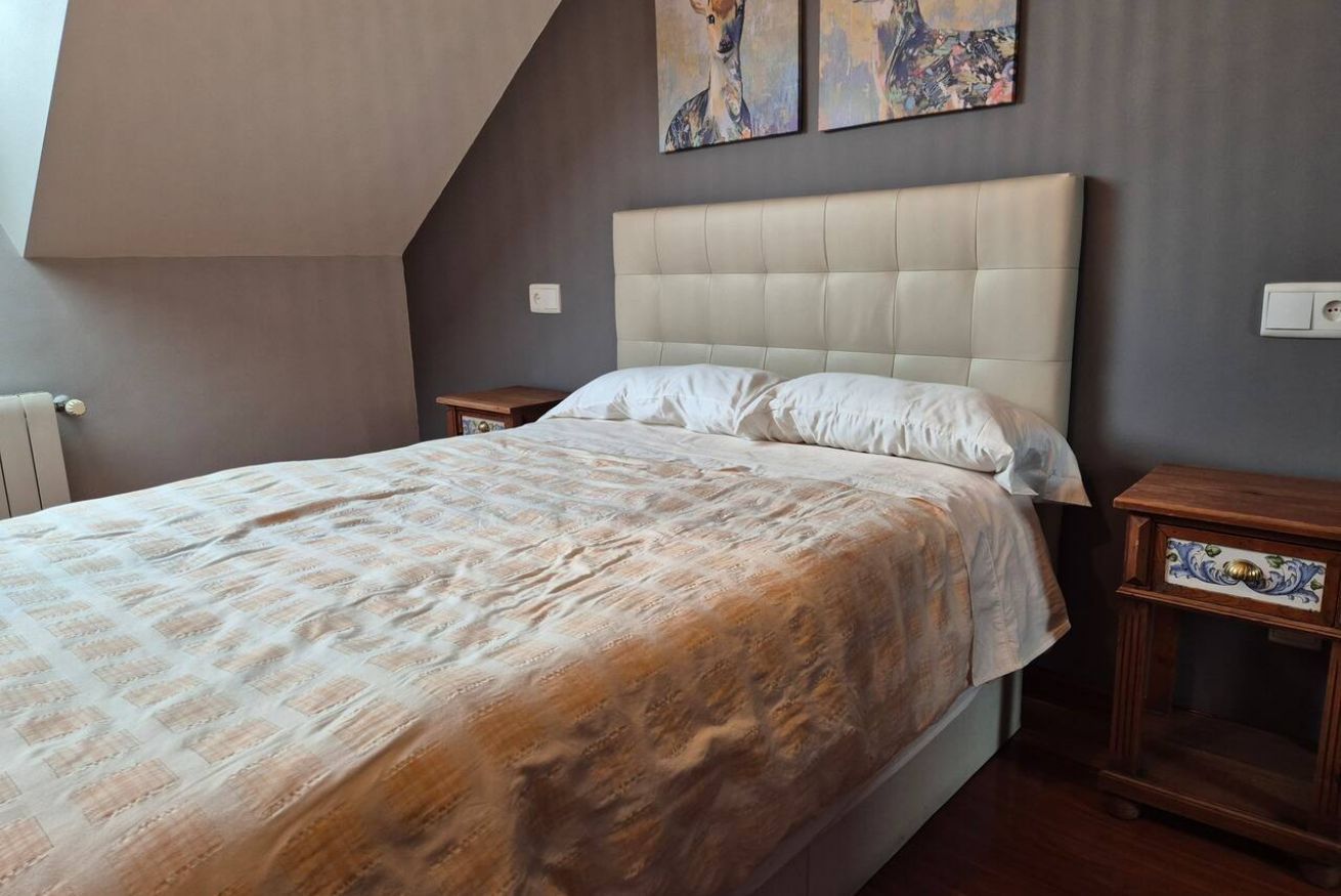 A bedroom with a large bed, a headboard, two nightstands, and artwork on the wall.